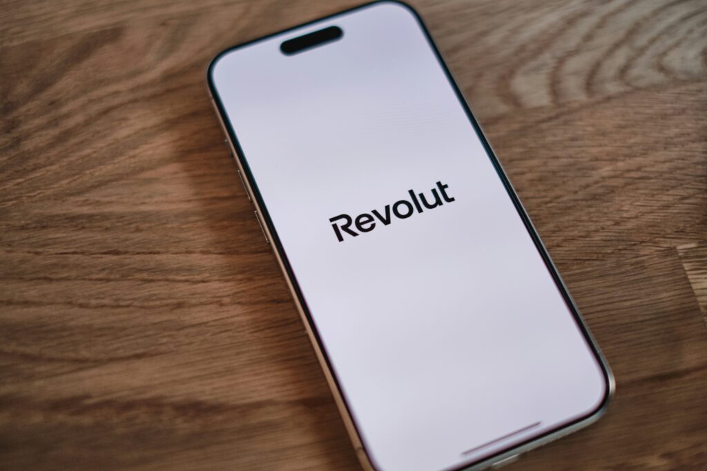A cell phone sitting on top of a wooden table with the logo "Revolut" displayed on it.
