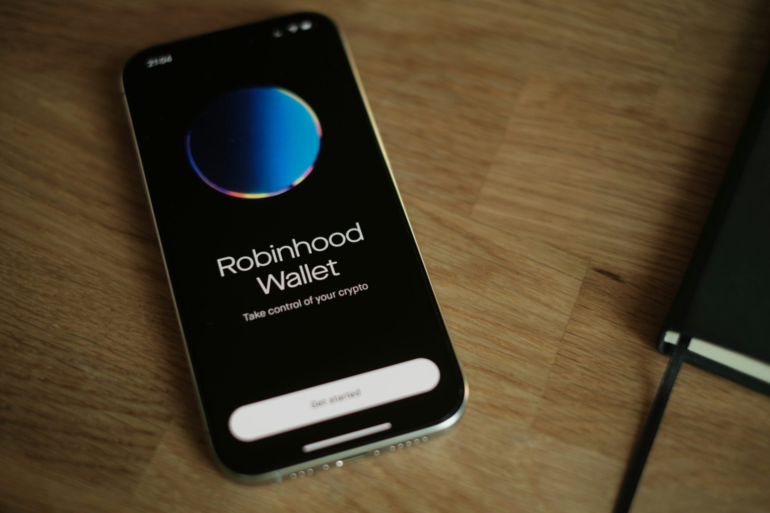 A cell phone on top of a wooden table with 'Robinhood Wallet' displayed on it.